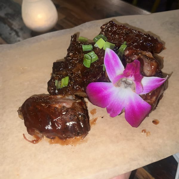 Glazed ribs with green onions and a purple orchid garnish on parchment paper.
